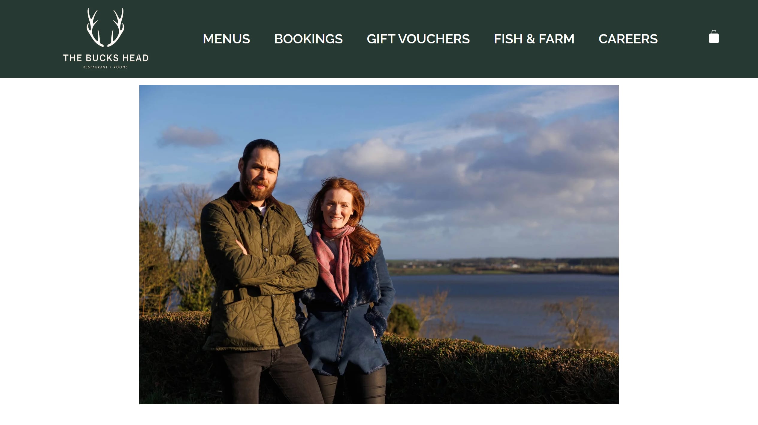 The Bucks Head's current homepage: a green header with the antler logo and five menu items above a full-width photograph of the owners by Dundrum Bay, with no headline, hours or booking action