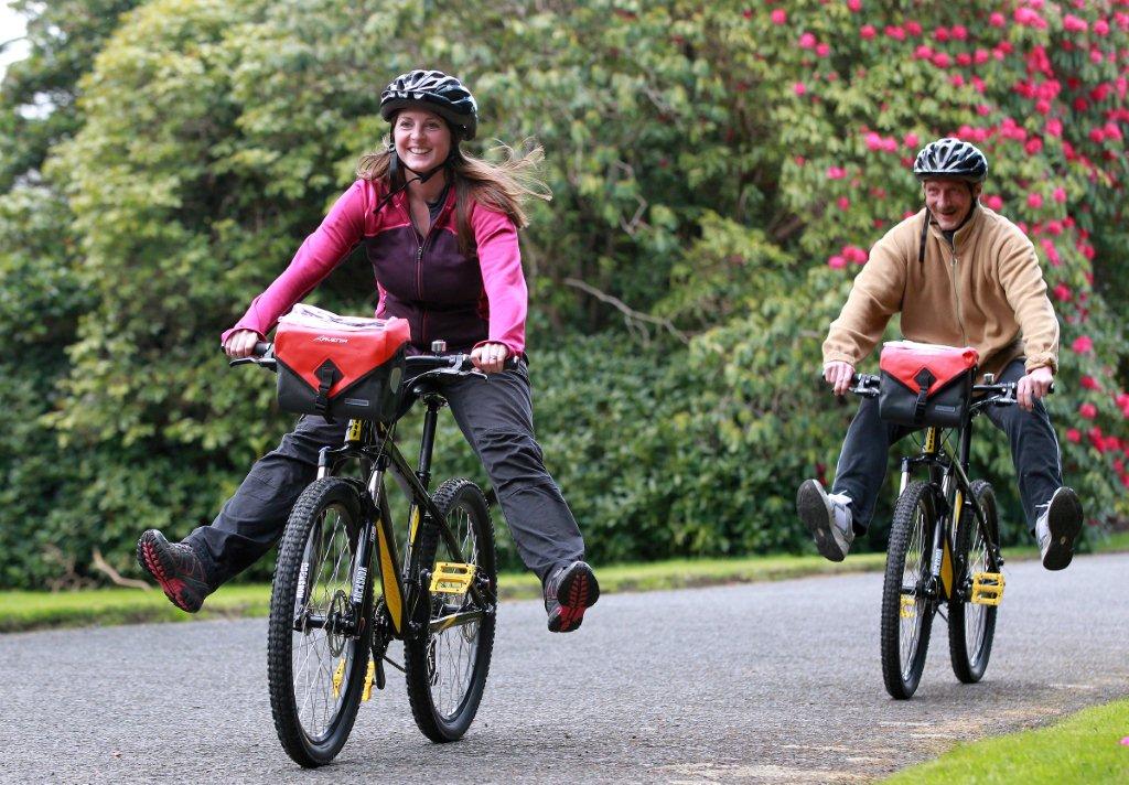 Two cyclists freewheel past the rhododendrons on hired bikes