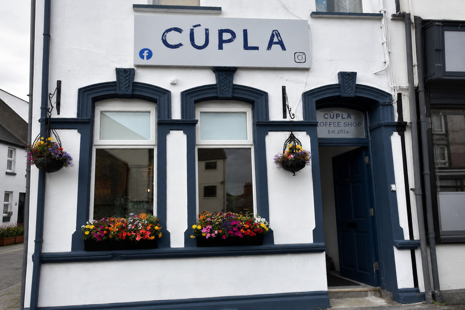 Faithful AI-generated visualisation of Cúpla's three-bay shopfront at 105 Main Street: white render with navy joinery, the painted CÚPLA fascia board, two hanging baskets, two window boxes and the Est. 2024 decal on the open navy door