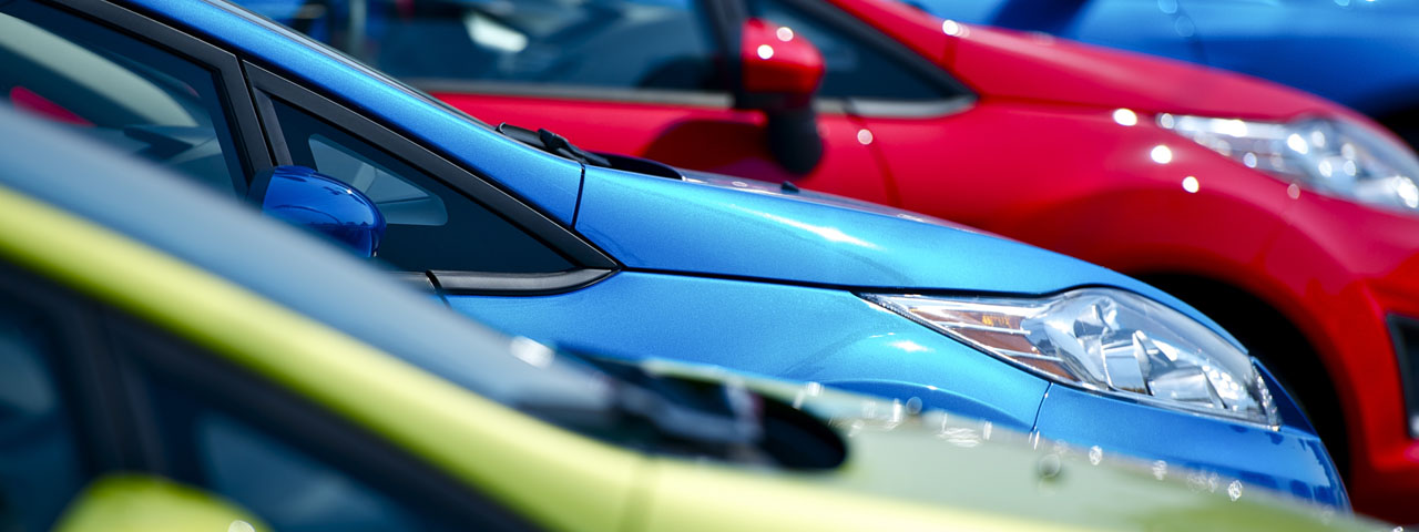 Blue, red and yellow cars lined up on a forecourt